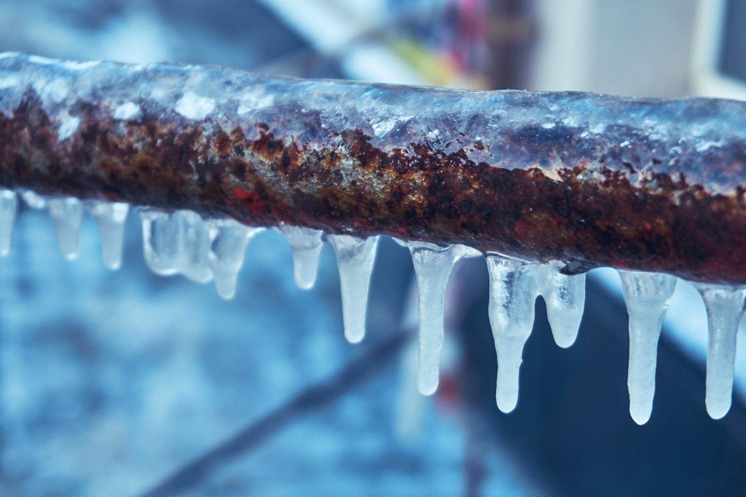 Frozen rusty pipe with icicles hanging from the bottom, showing effects of winter plumbing issues.